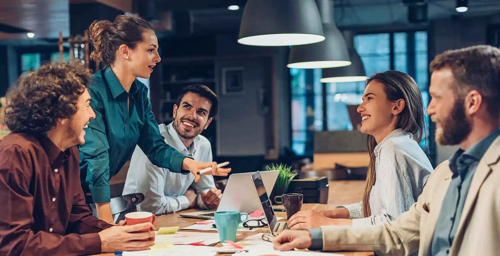 Diverse team of five professionals engaging in a collaborative discussion around a table in a modern office setting.