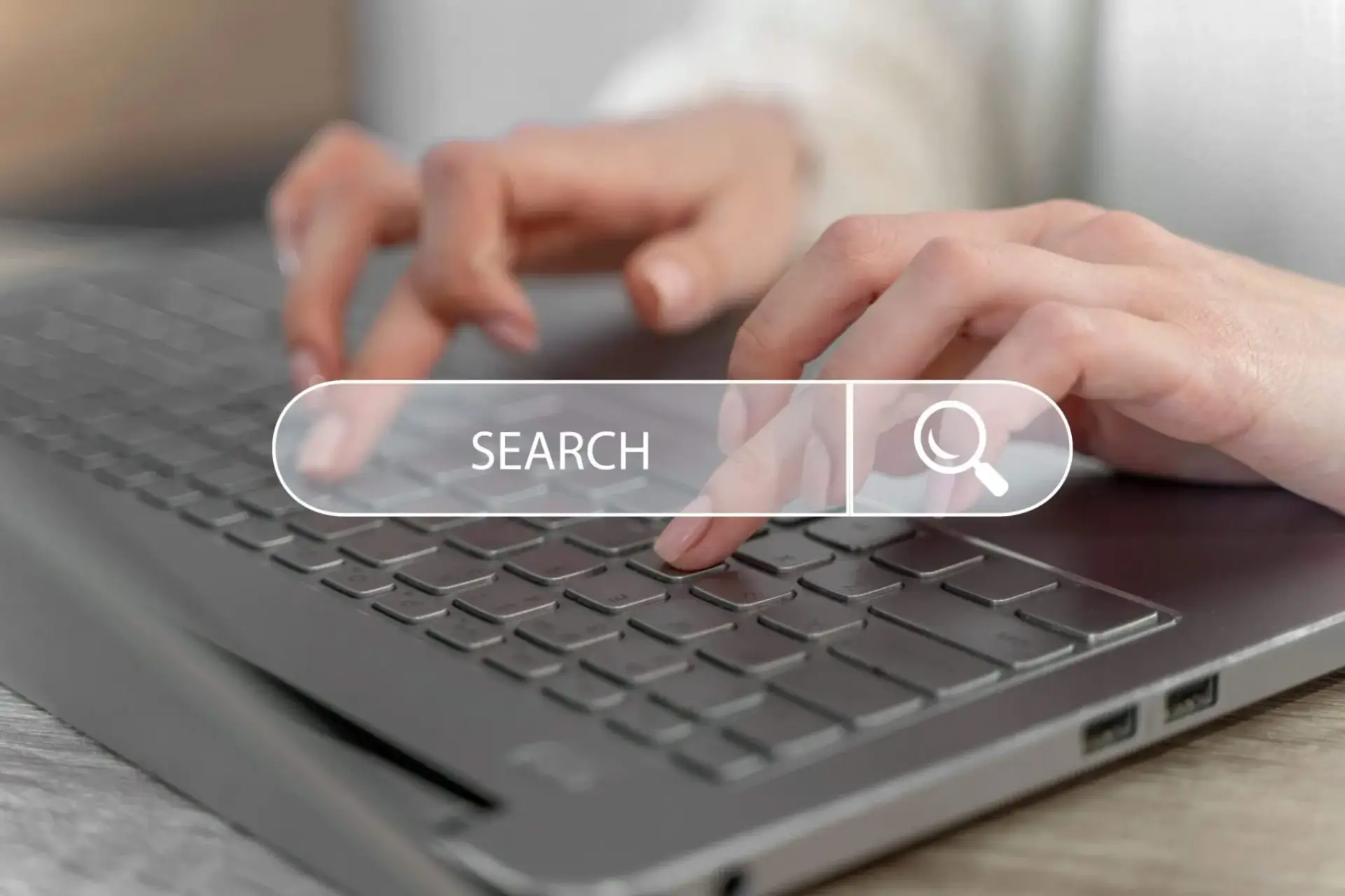 Close-up of a person's hands typing on a laptop keyboard with a search bar graphic displaying 'SEARCH' and a magnifying glass icon, symbolizing online search capabilities at Bnternet.