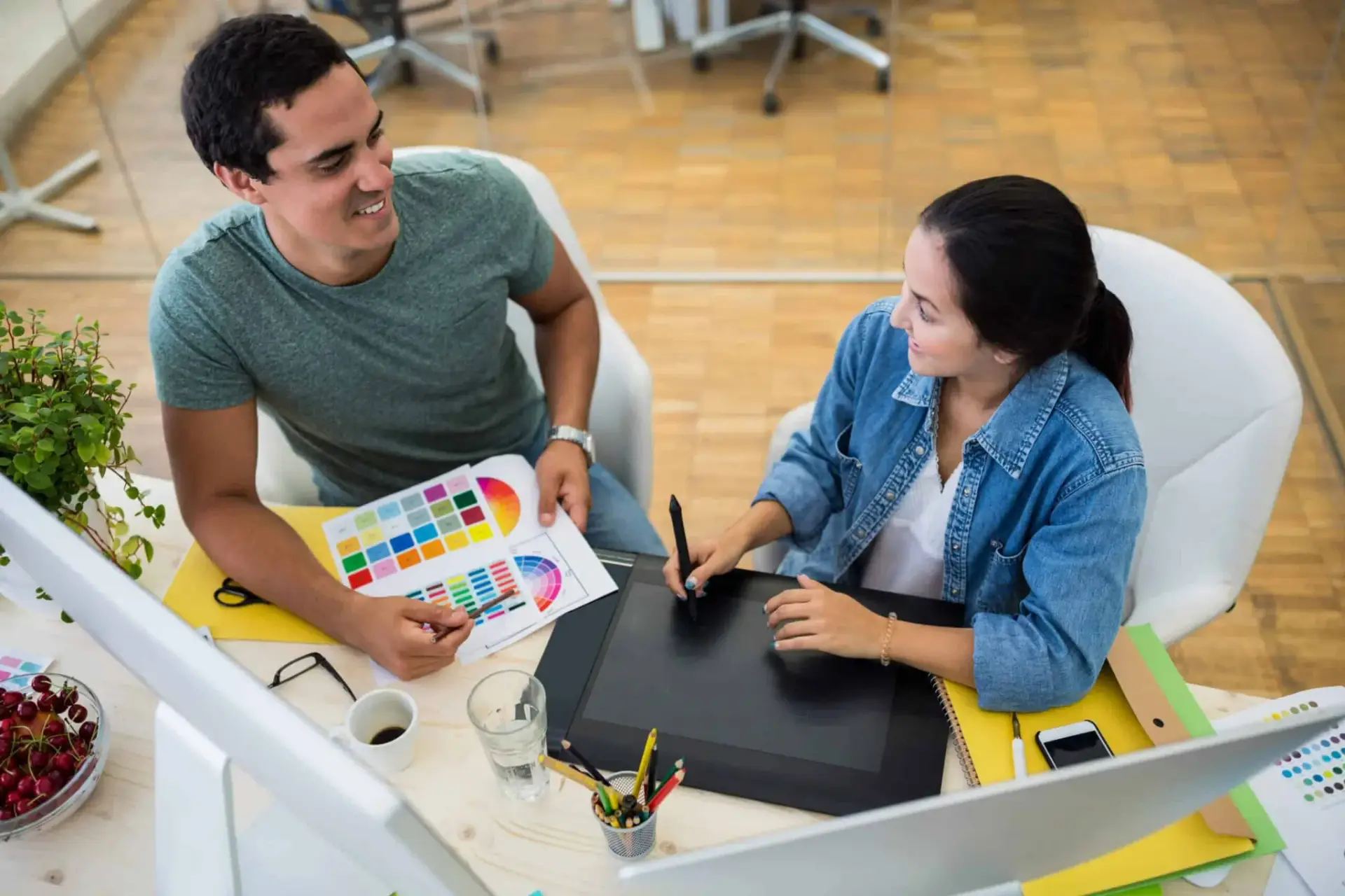 Two graphic designers, a man and a woman, collaborating over a digital drawing tablet with color swatches in a bright office at Bnternet